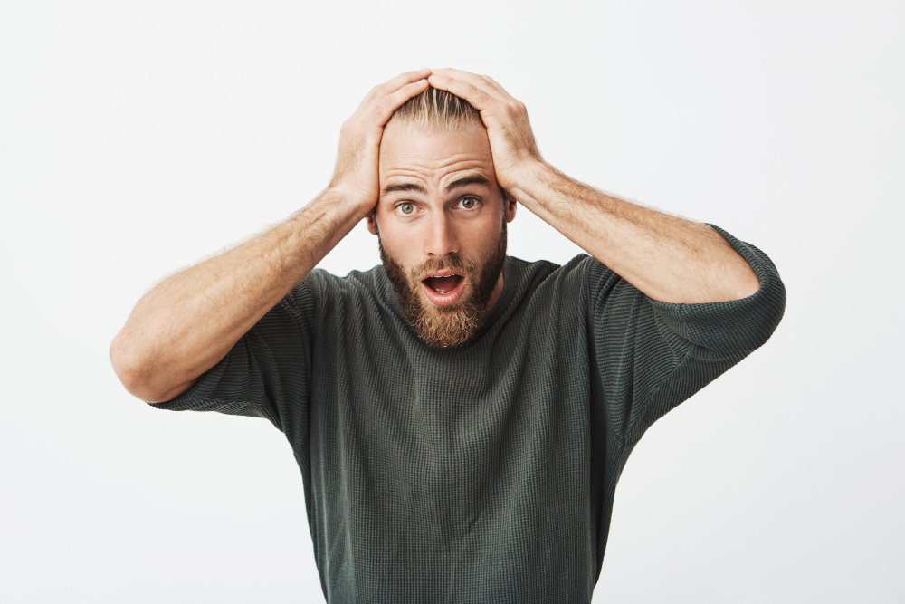 Homem com expressão de stress e mãos na cabeça, ilustrando impacto emocional e psicológico na queda de cabelo