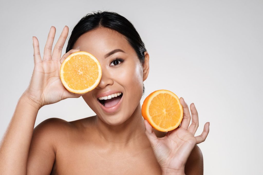 Mulher com laranja representando vitamina C e colagénio para cabelo
