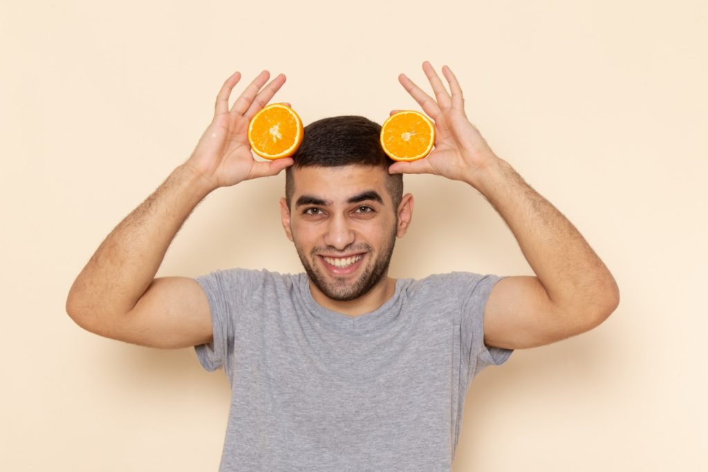 Homem a segurar frutas cítricas representando vitaminas para queda de cabelo
